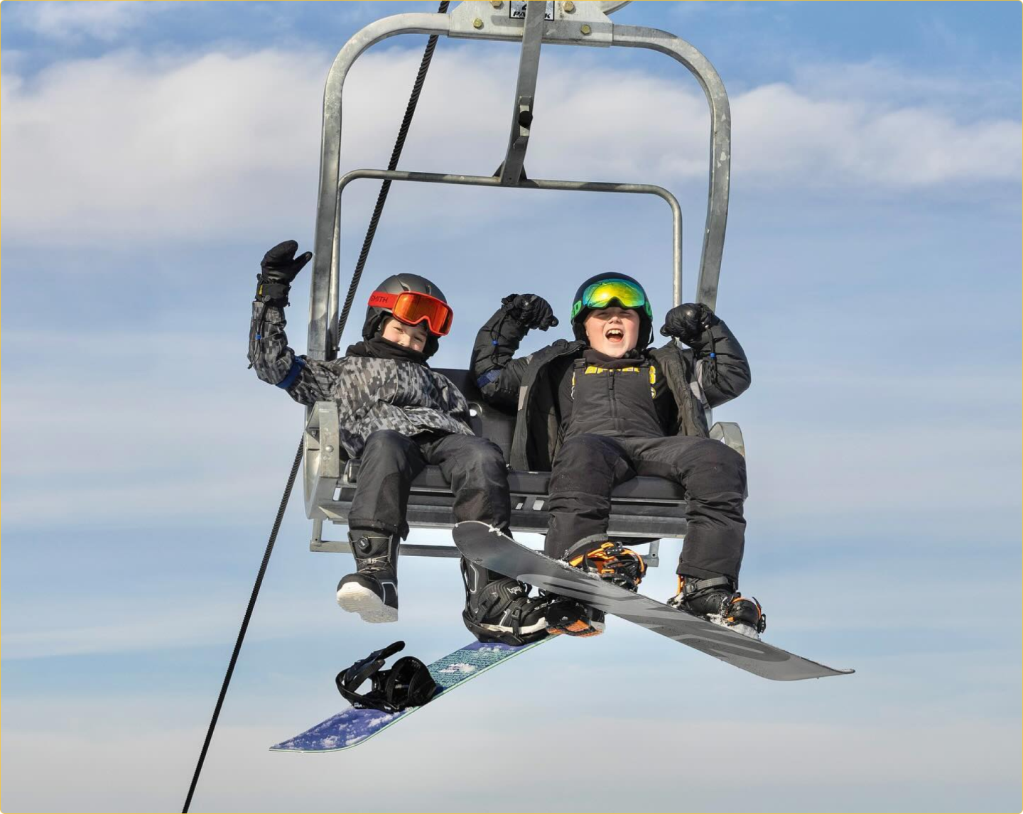 two kids on chairlift, comically flexing their muscles