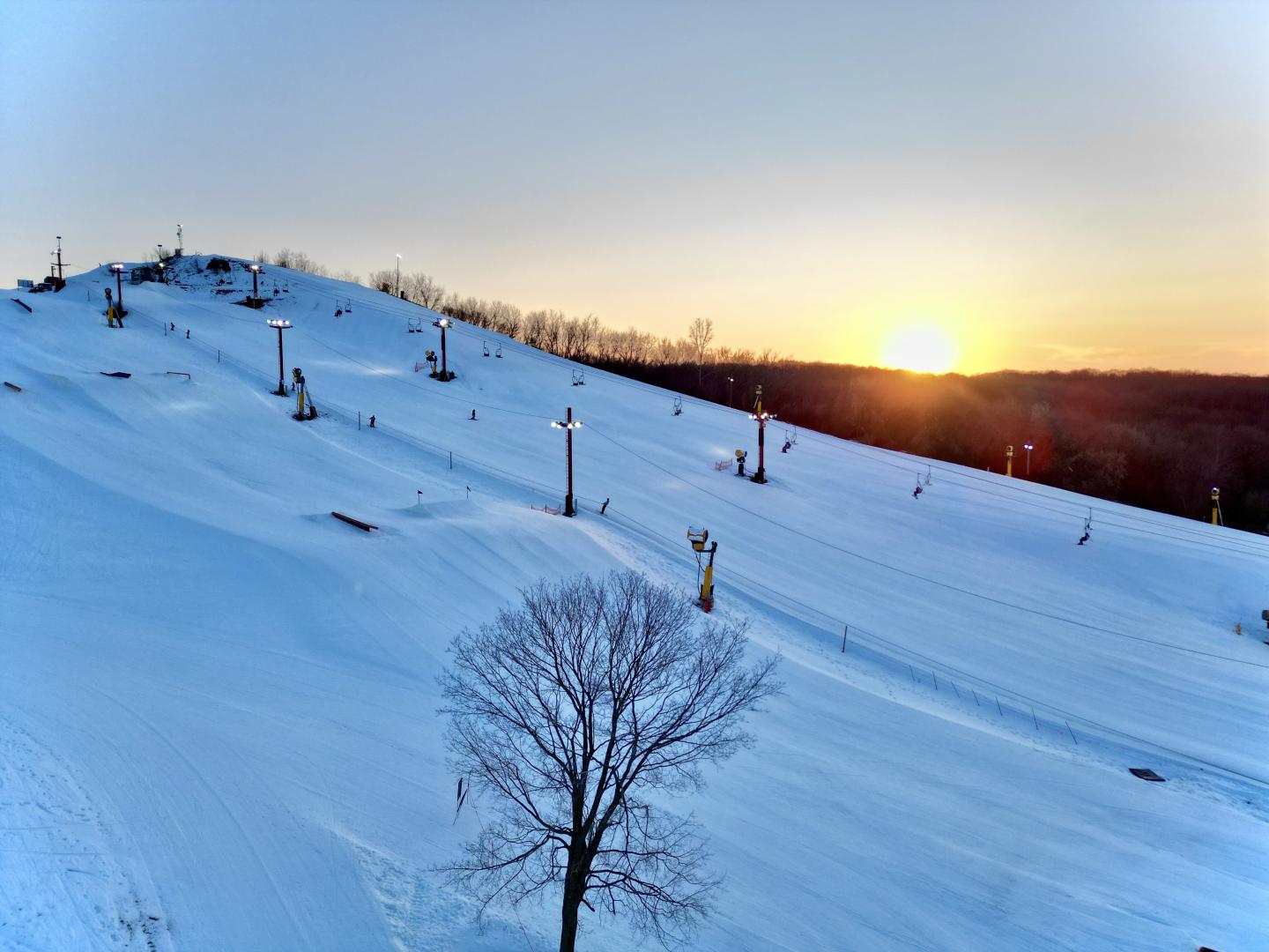 Drone shot of ski hill with chair lift, and sunset behind it
