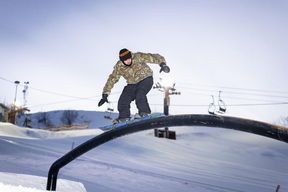 Snowboarder grinding on a rail in a snowy landscape.