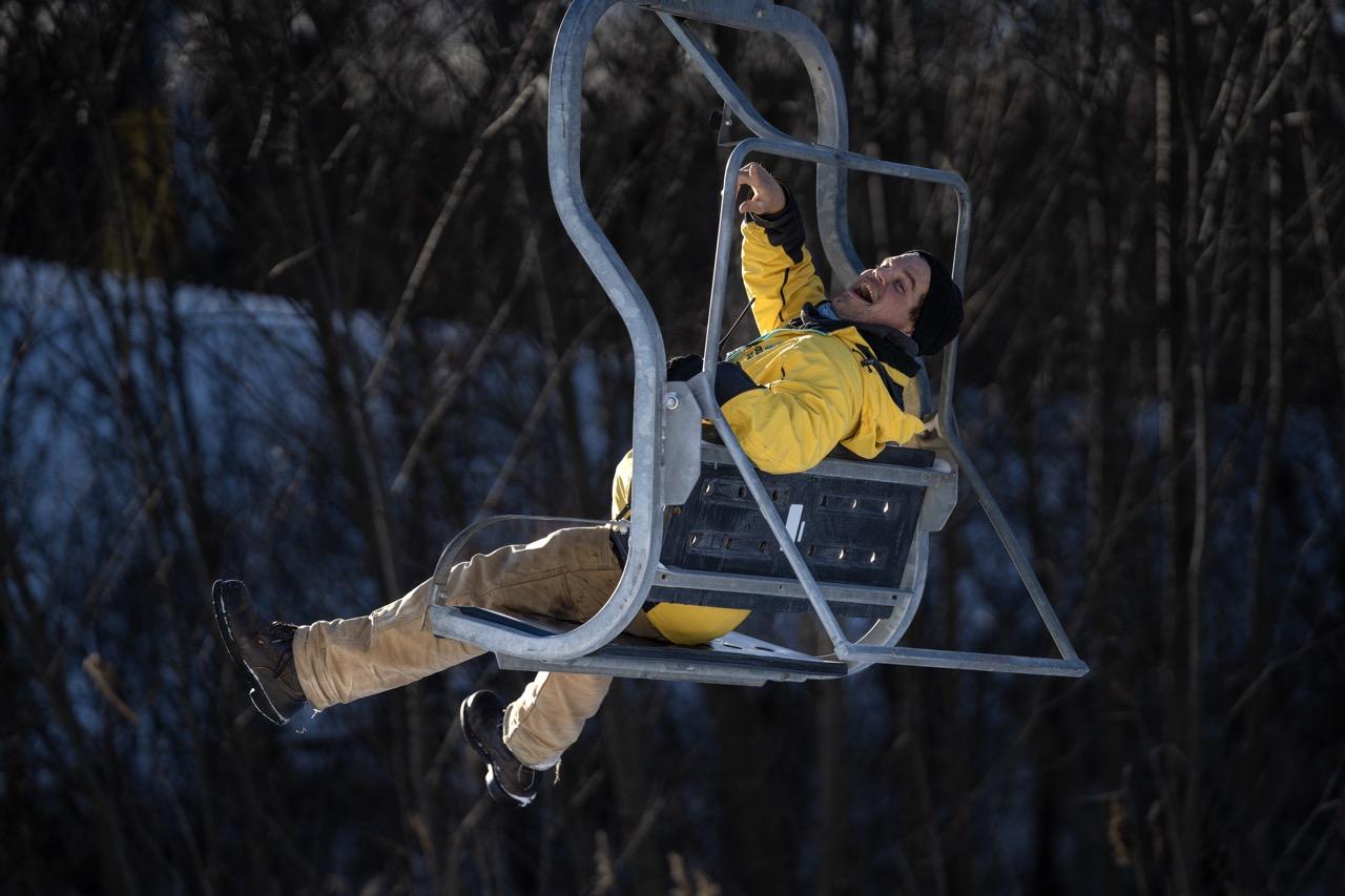 Person in a yellow jacket riding a ski lift over snowy forest.