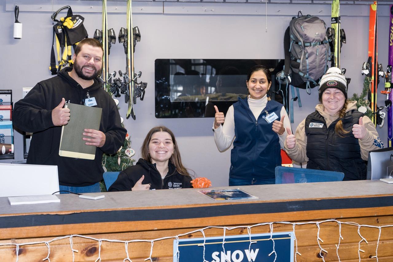 Four shop staff smile and give thumbs-up behind a counter in a workshop.