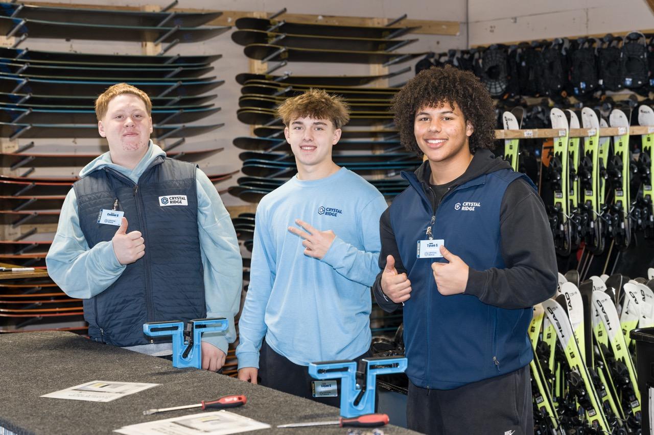 Three young men in sportswear stand in a ski equipment workshop.