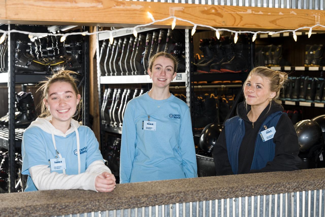 Three smiling women behind a counter at a horse tack shop.