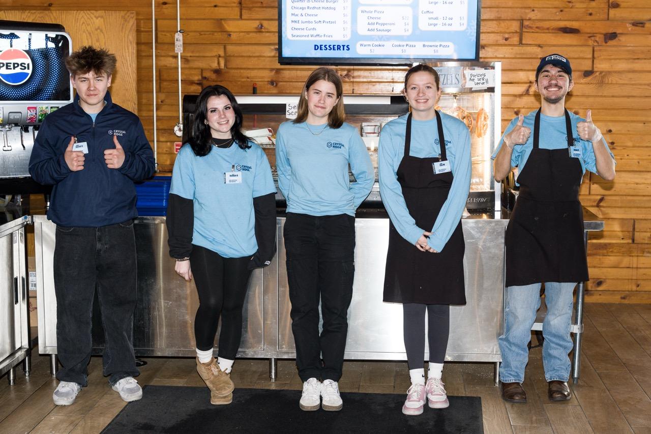 Five café staff members in blue shirts and aprons stand smiling behind a counter.