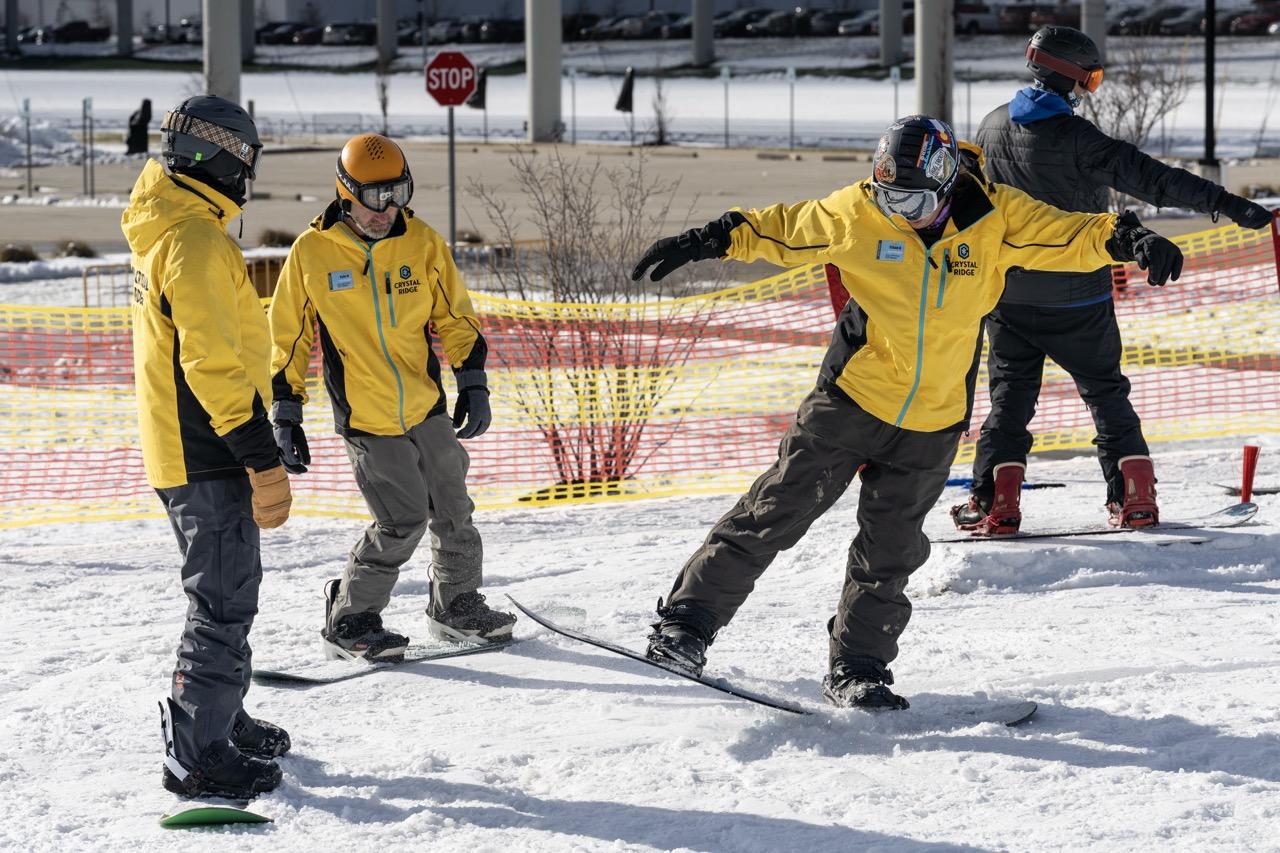 Snowboarders in yellow jackets practicing on a snowy slope.