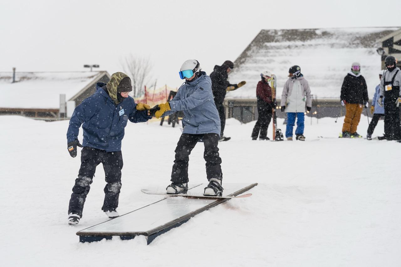 Two snowboarders practicing on a snowy slope as others watch.