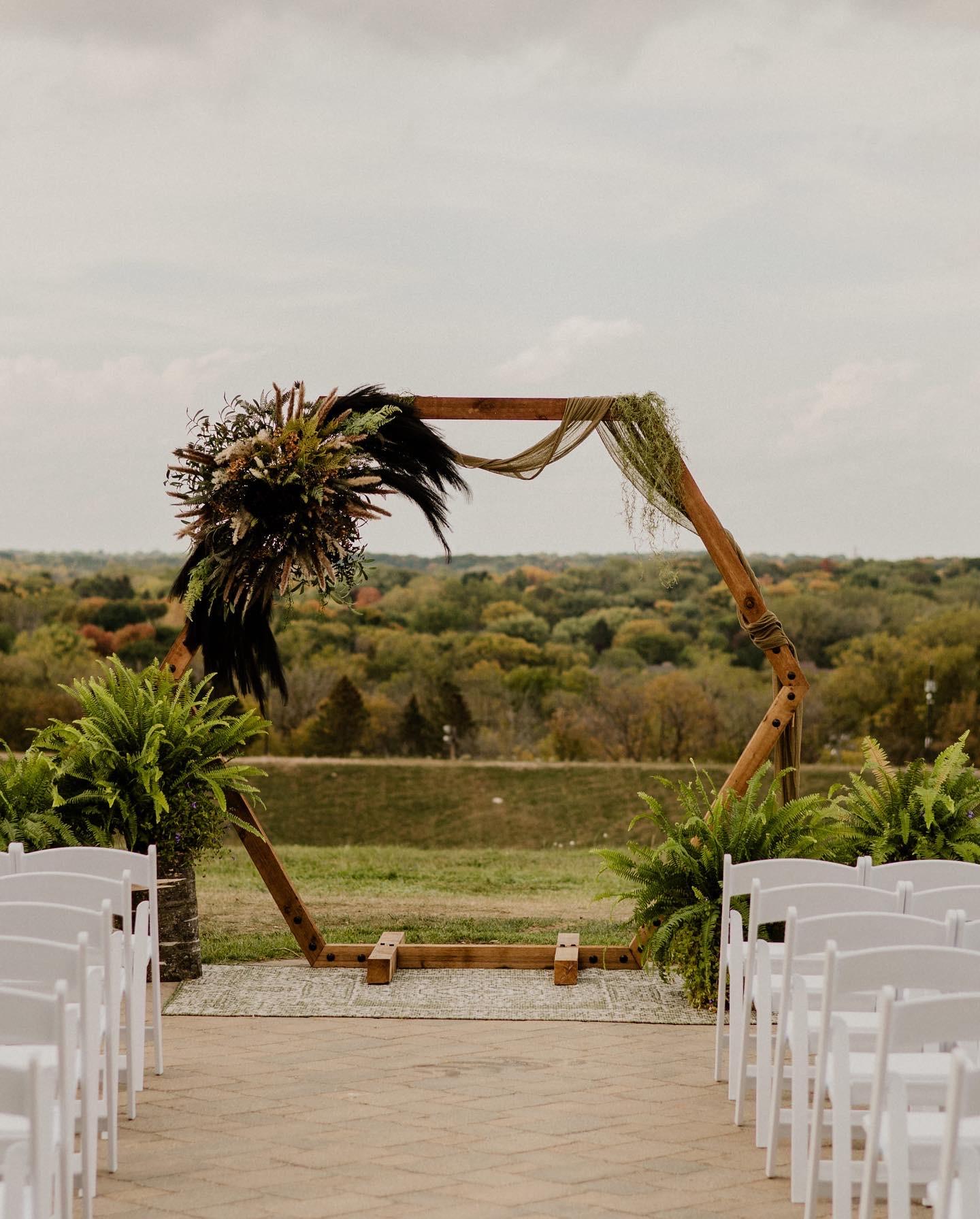 Rustic wooden wedding arch with palm fronds overlooking a vineyard.