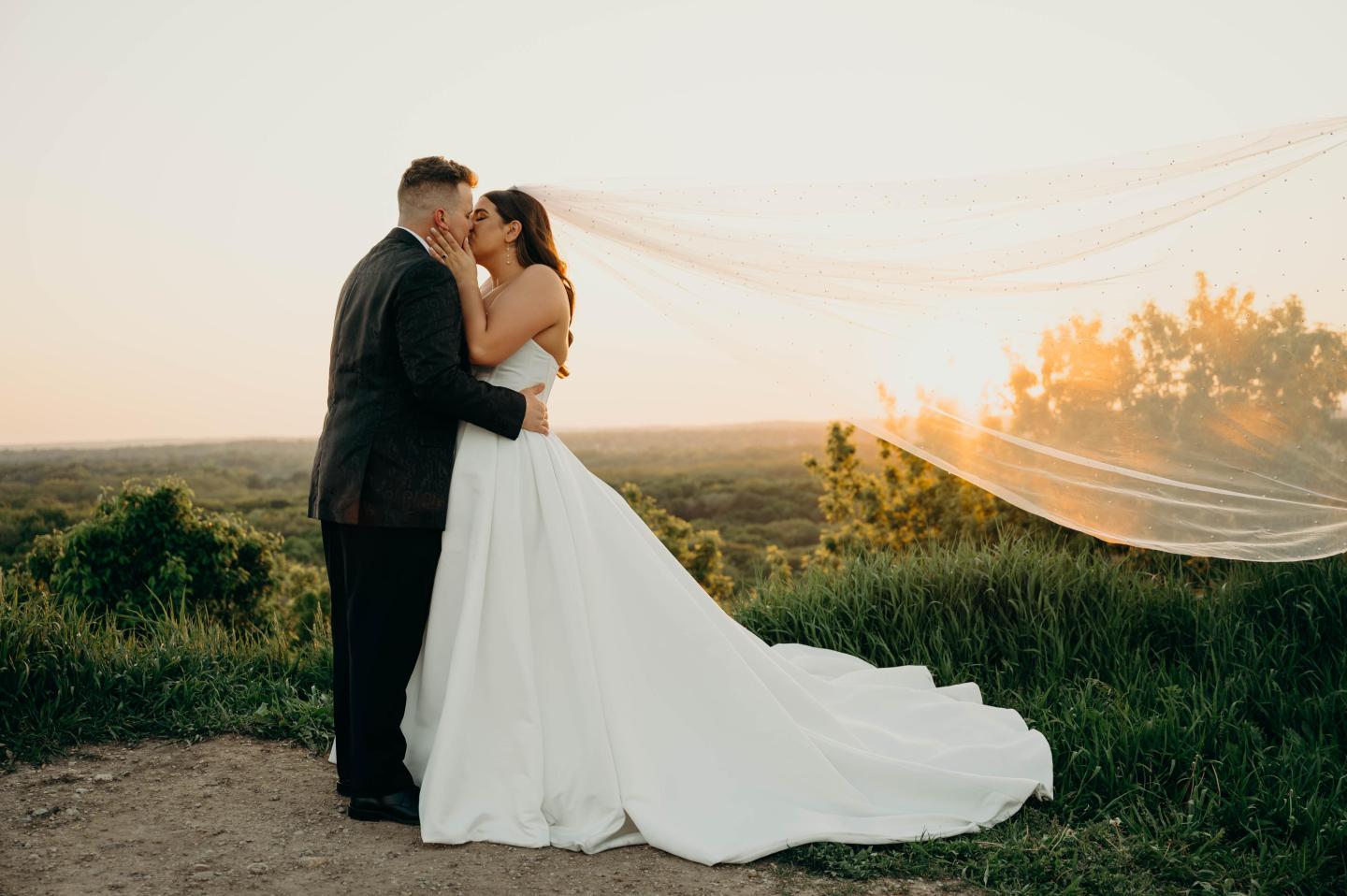 Bride and groom embrace at sunset beside flowing white fabric.