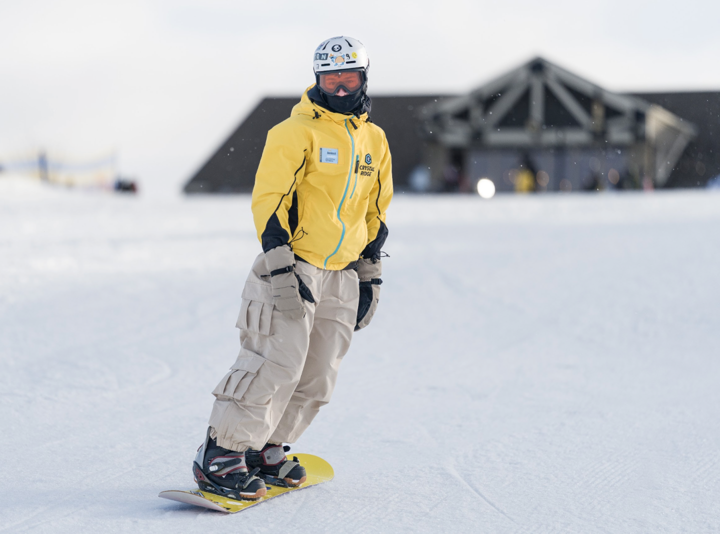 Snowboarder in yellow jacket riding on a snowy slope near a lodge.