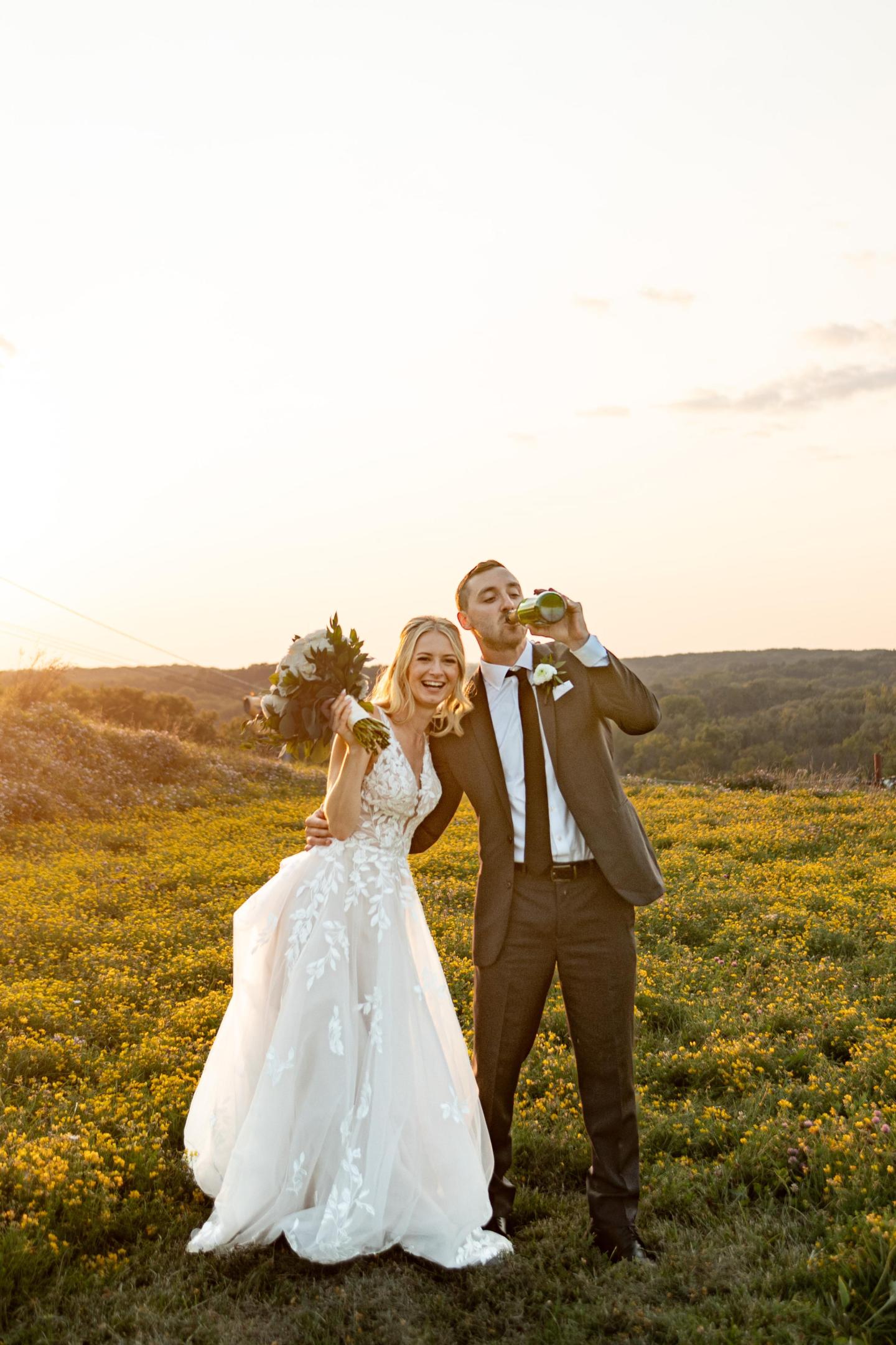 Bride and groom embrace in a sunlit field at sunset.