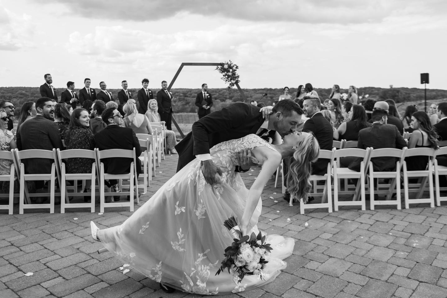 Black-and-white wedding photo of groom dipping bride outdoors.