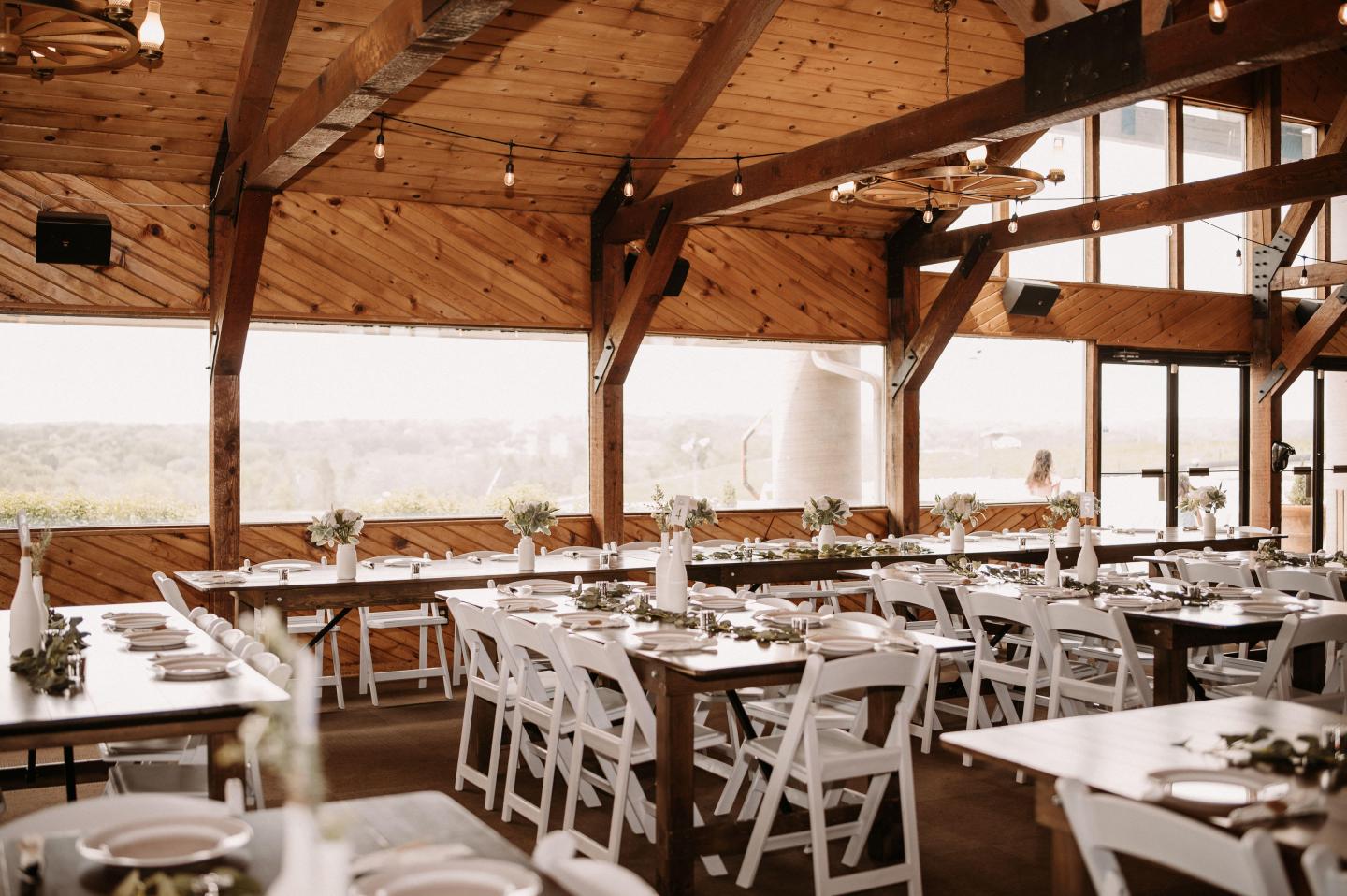 Rustic open-air wedding reception with white tables and chairs under wooden beams