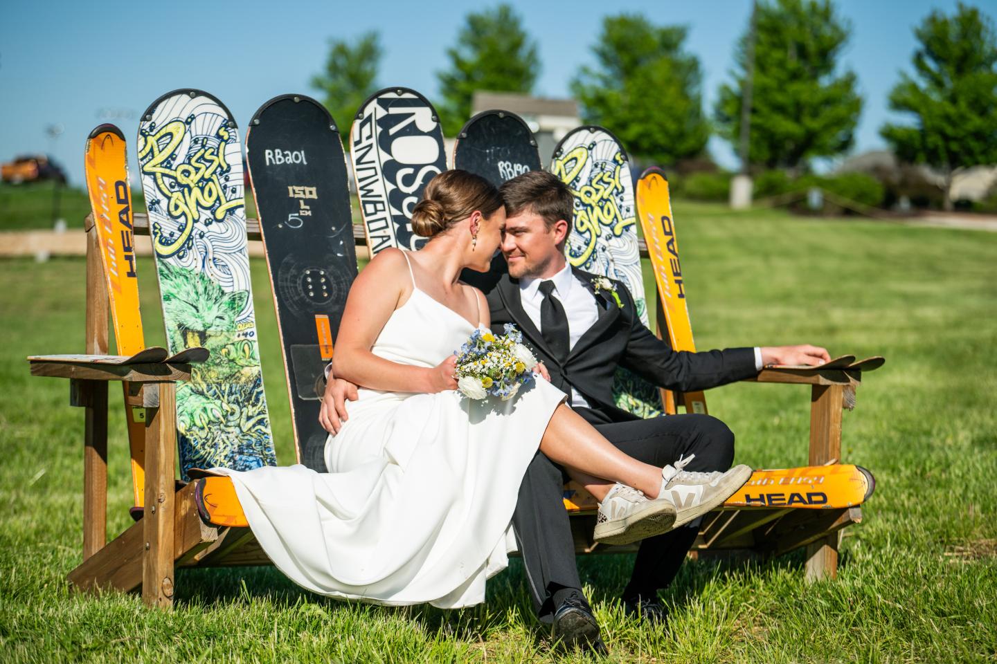 Bride and groom sitting on a yellow bench in a grassy park.