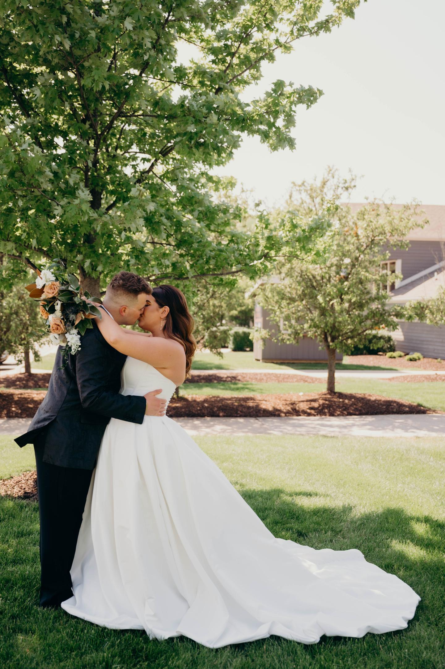 Bride and groom embrace outdoors, her white gown flowing across the grass.