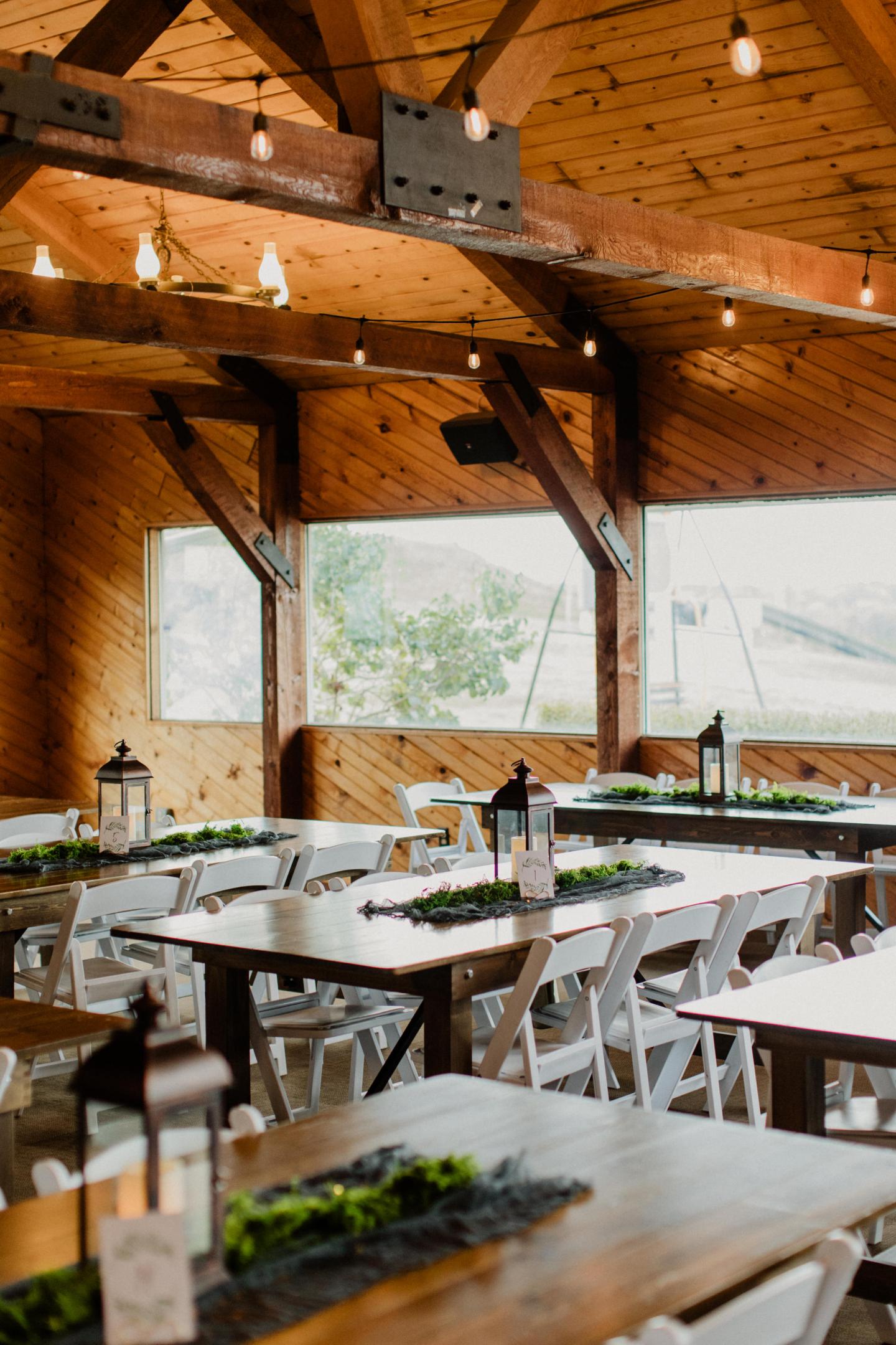 Rustic wooden restaurant interior with long tables and large windows overlooking greenery.