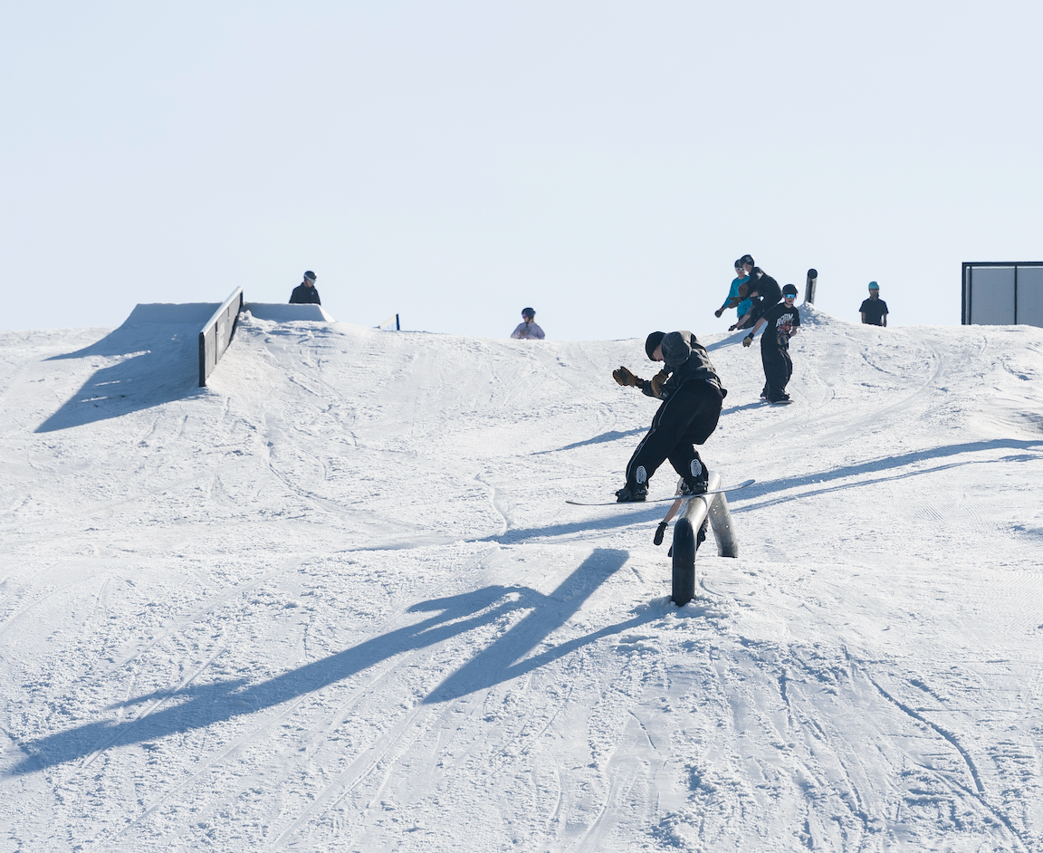 Snowboarder performing a jump on a snowy slope, with others in the background.