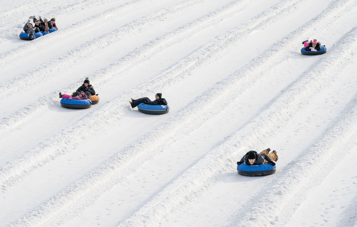 Aerial view of people riding snow tubes down parallel snowy lanes.