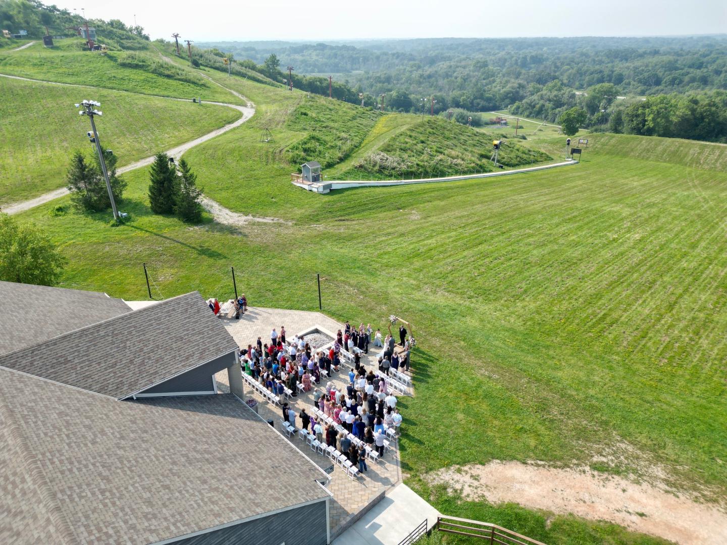 Aerial view of people gathered beside a rural building amid green fields.