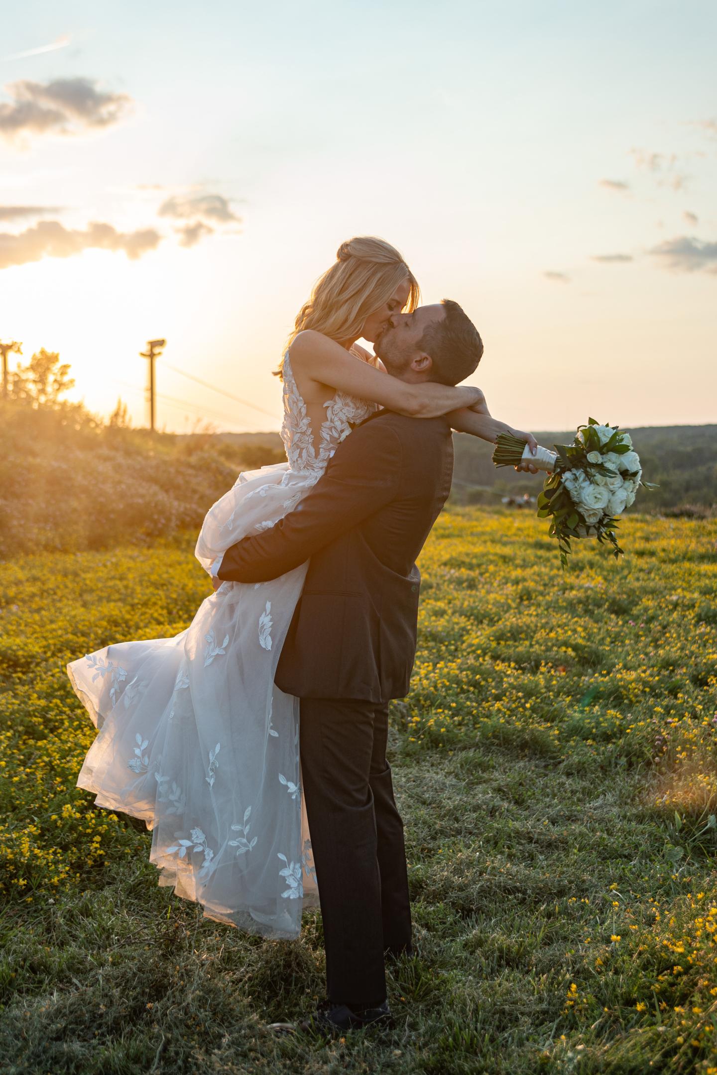 Bride and groom embracing in a sunlit field at sunset.