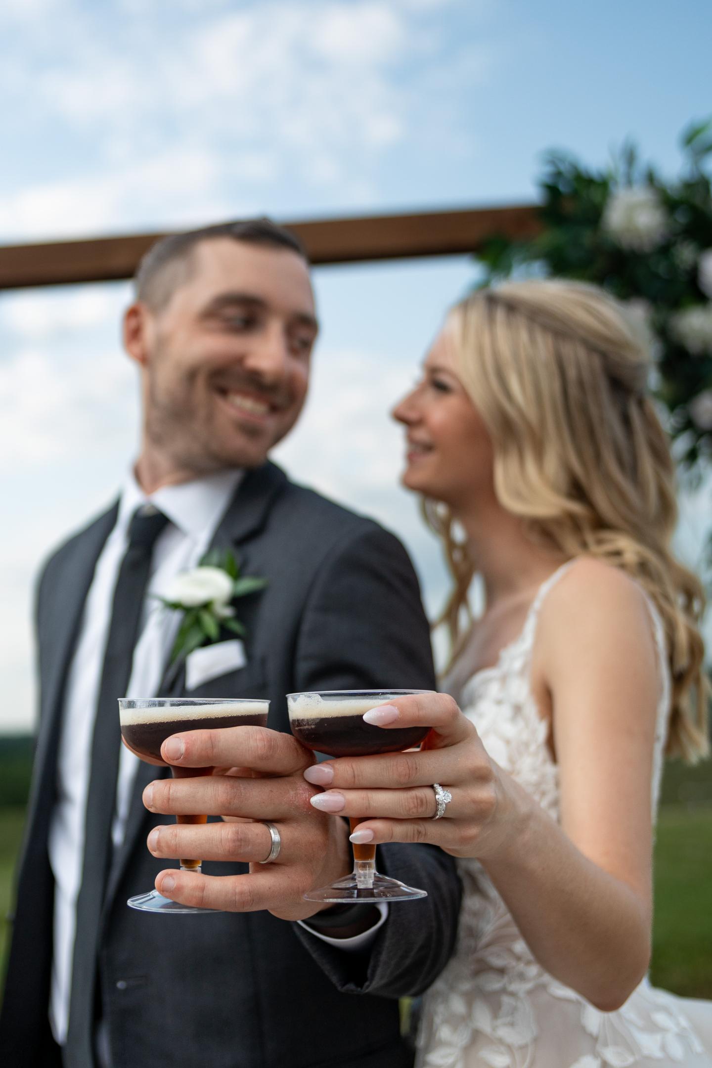 Bride and groom smiling, holding espresso martinis at an outdoor wedding